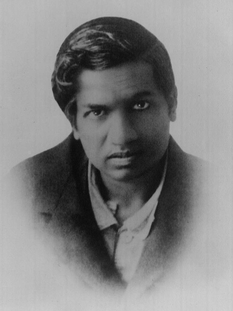 Potret hitam putih Srinivasa Ramanujan, matematikawan legendaris asal India yang mengenakan jas dan dasi kupu-kupu di awal abad ke-20.